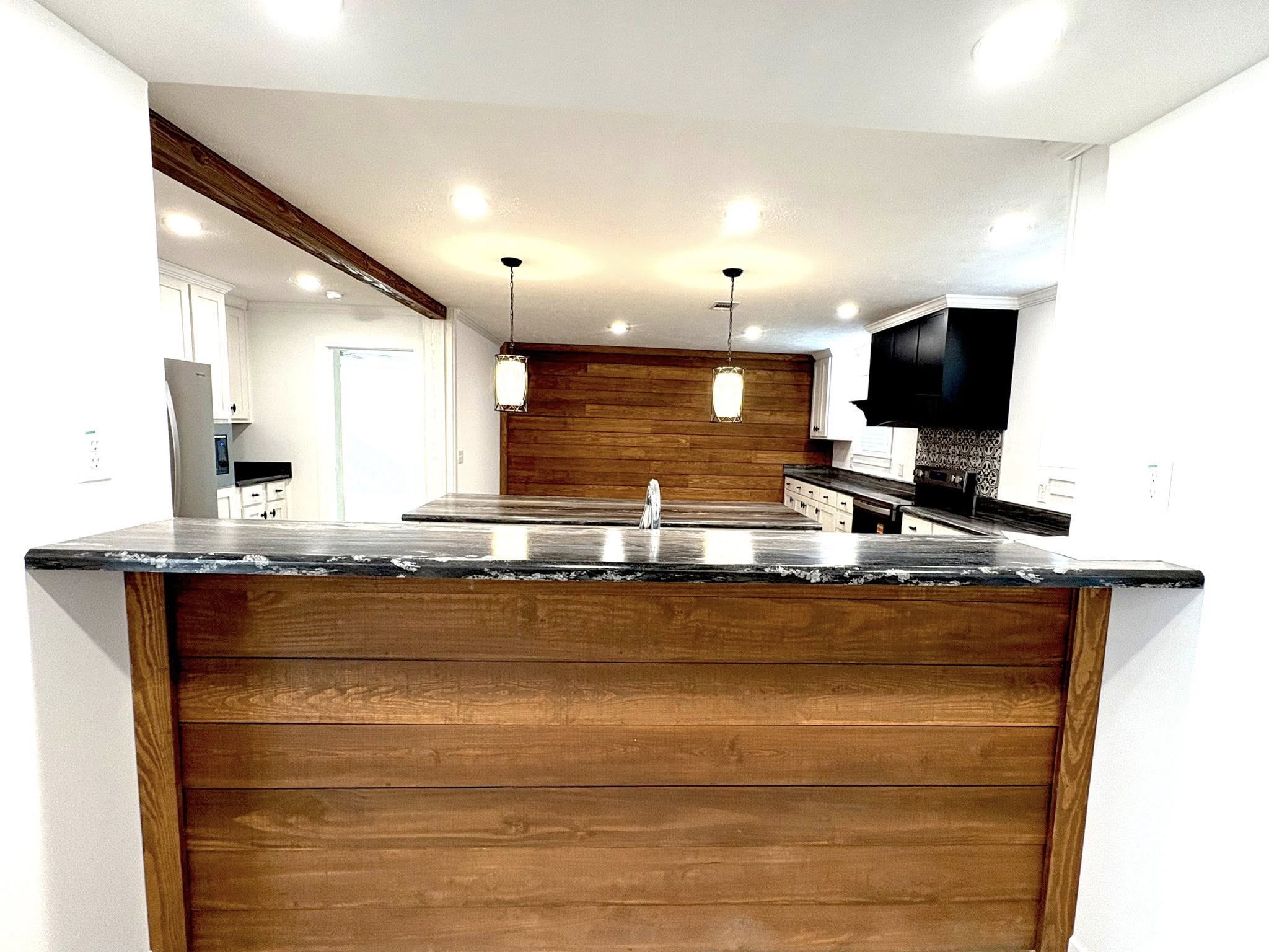Spacious kitchen with wood paneling, black countertops, and hanging pendant lights. White cabinetry, modern appliances, and a welcoming ambiance.