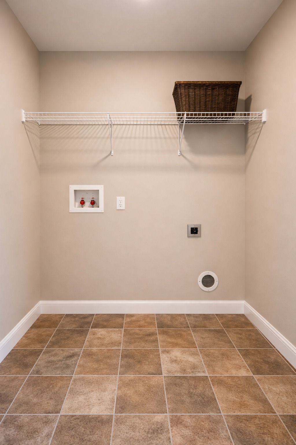 Empty laundry room with beige walls, tile floor, and a white wire shelf. A brown wicker basket sits on the shelf, under warm lighting. Minimalist and clean.