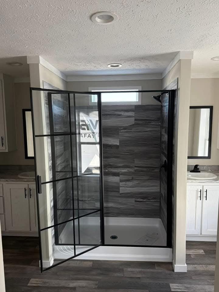 Modern bathroom with a glass shower featuring black frames and gray tiles. It is flanked by white cabinets with sinks, creating an elegant vibe.