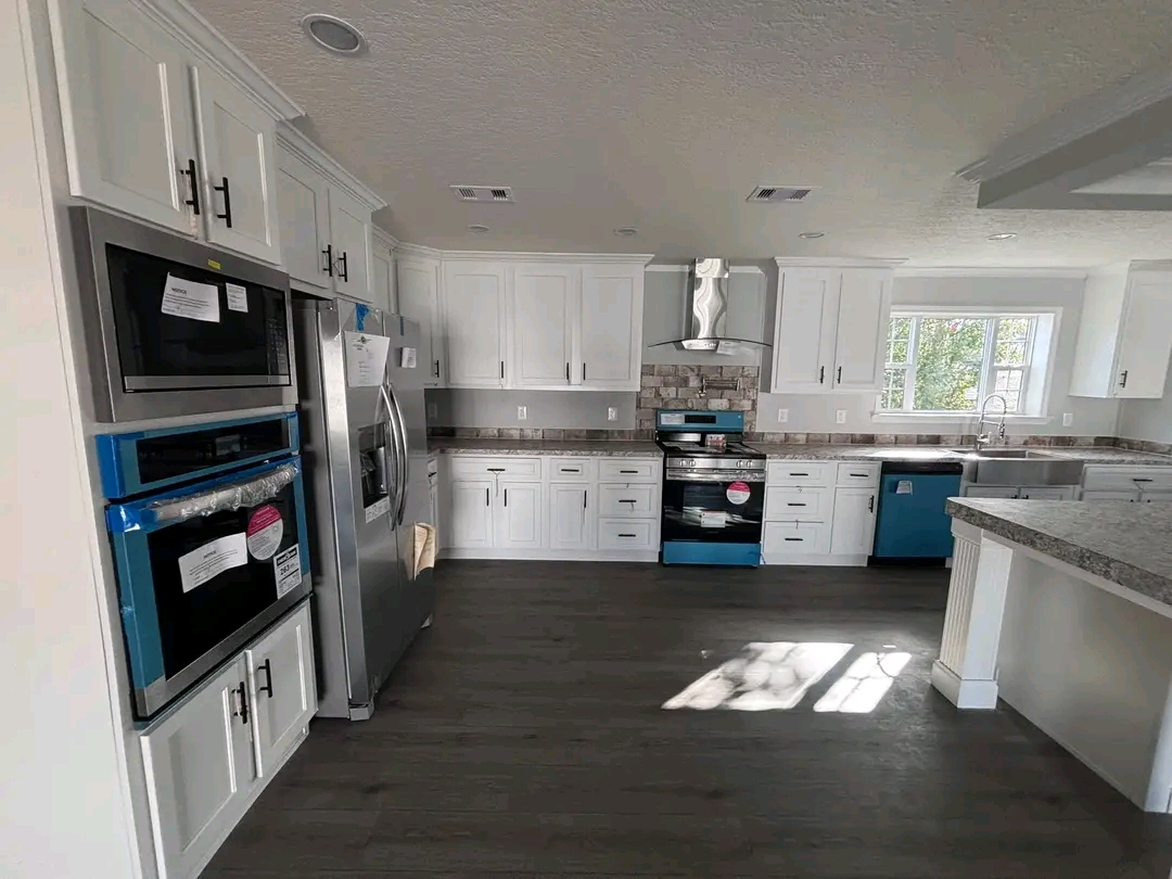 Bright modern kitchen with white cabinets, stainless steel appliances, and granite countertops. Sunlight streams through a window, creating a warm and inviting atmosphere.