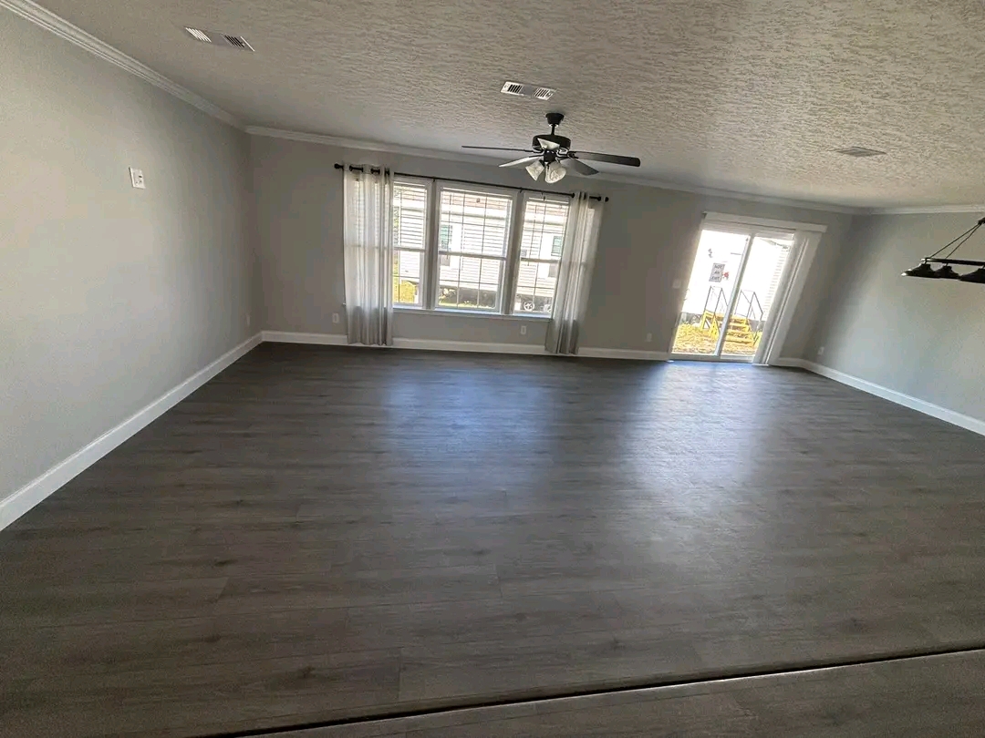 Spacious empty living room with smooth gray flooring and light gray walls. Large windows and sliding glass doors allow natural light, creating an airy atmosphere.