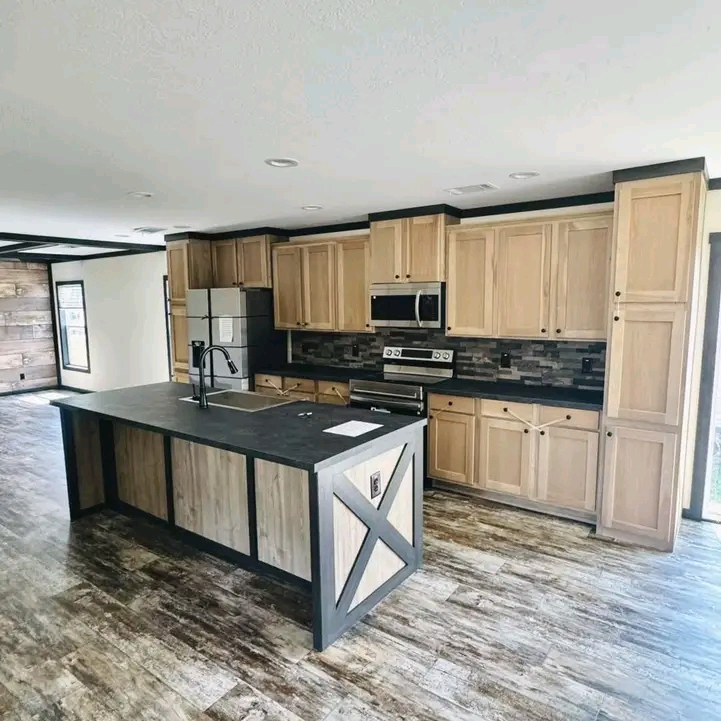 Modern kitchen with rustic wood cabinetry, black countertops, and an island with a built-in sink. Stainless steel appliances accent the space.