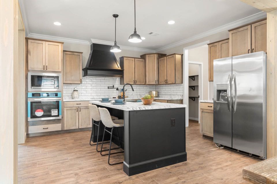Modern kitchen with light wood cabinets, a black island, and white marble countertops. Stainless steel appliances add a sleek touch. Bright, inviting ambiance.