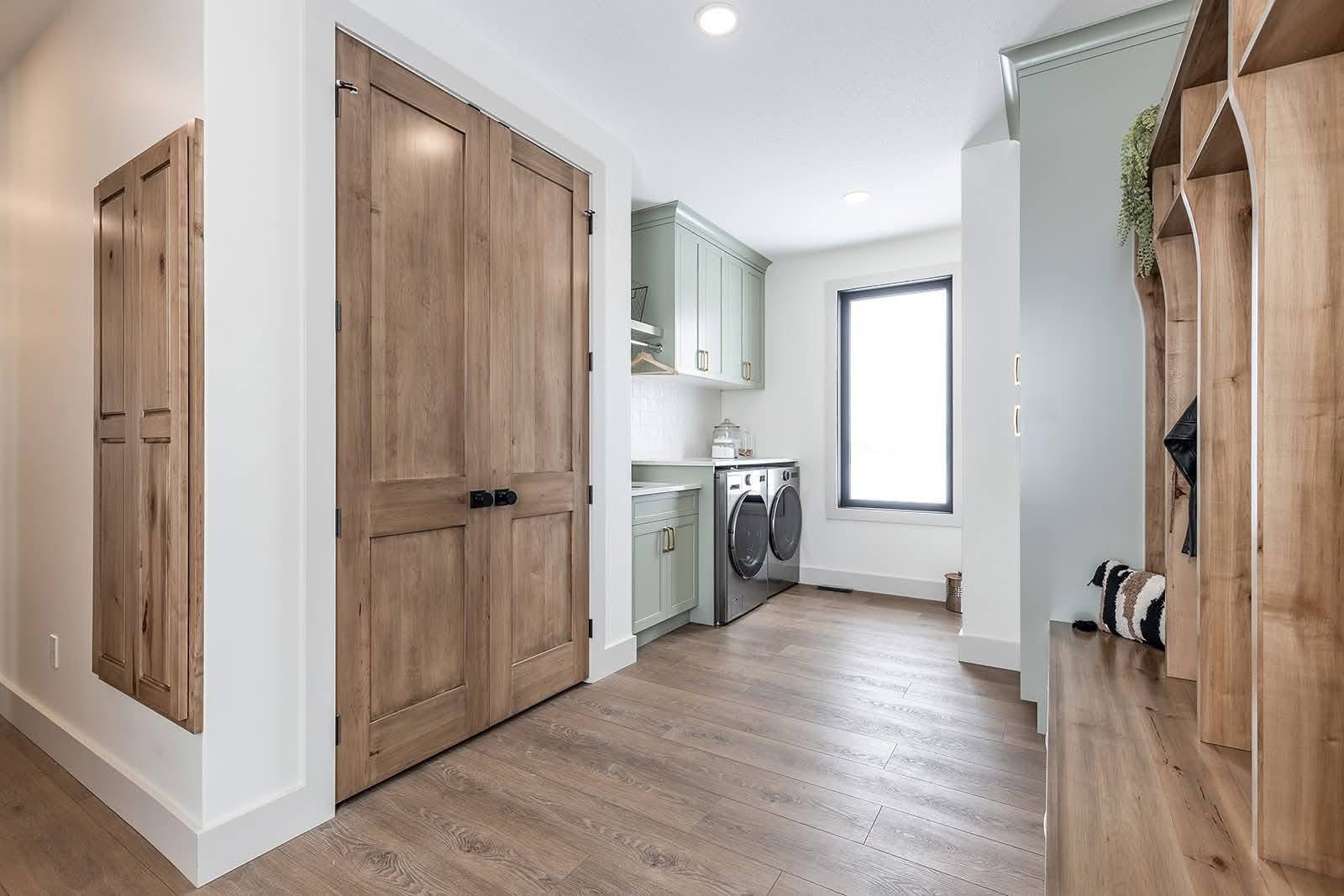 Modern laundry room with green cabinets, washer, and dryer. Light wood flooring and accents; a cozy, organized space with a serene, tidy vibe.