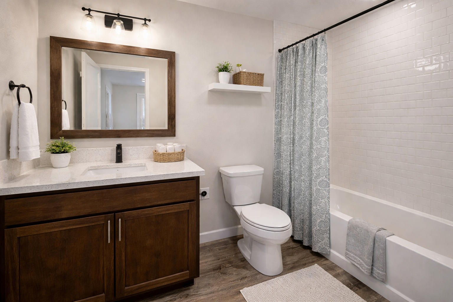 A modern bathroom with a wood vanity and mirror, a white countertop, and a potted plant. It features a white toilet, a shower with a blue curtain, and a cozy ambiance.