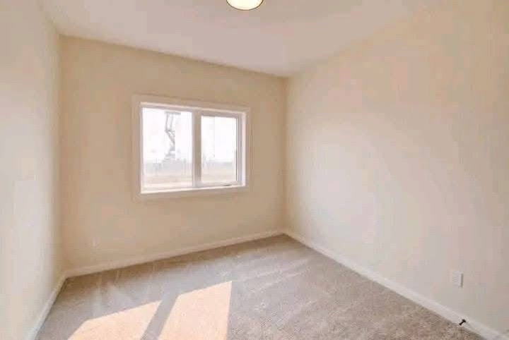 Small, empty room with beige walls and carpet, a single window showing bright sunlight, creating a warm and inviting atmosphere. Minimalist and calm setting.