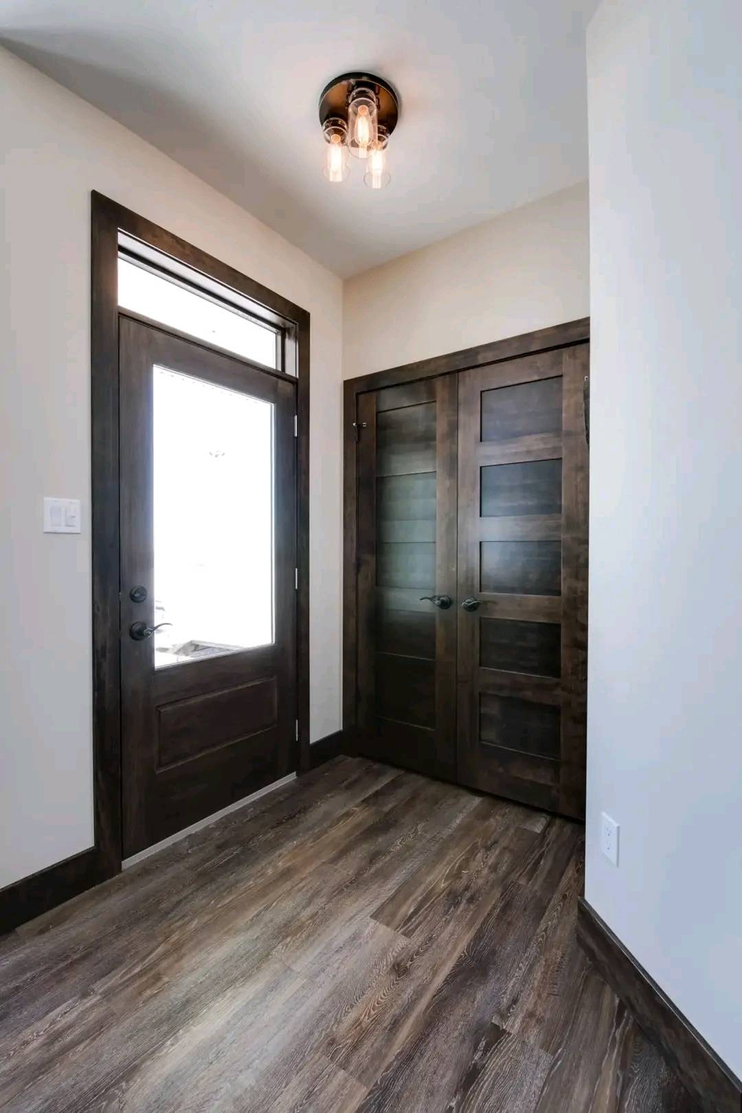 Simple, modern entryway with dark wood door and closet, illuminated by a ceiling light. Hardwood floors and neutral walls create a warm, inviting feel.