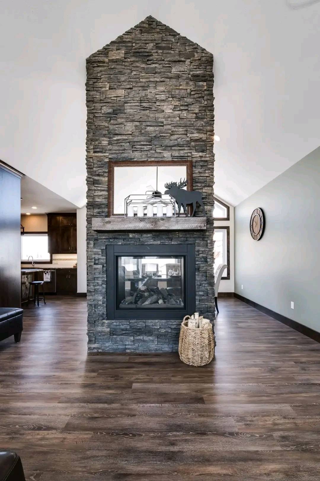Modern living room with a tall stone fireplace dividing the space. Wooden floors, soft lighting, and rustic decor create a cozy, welcoming atmosphere.
