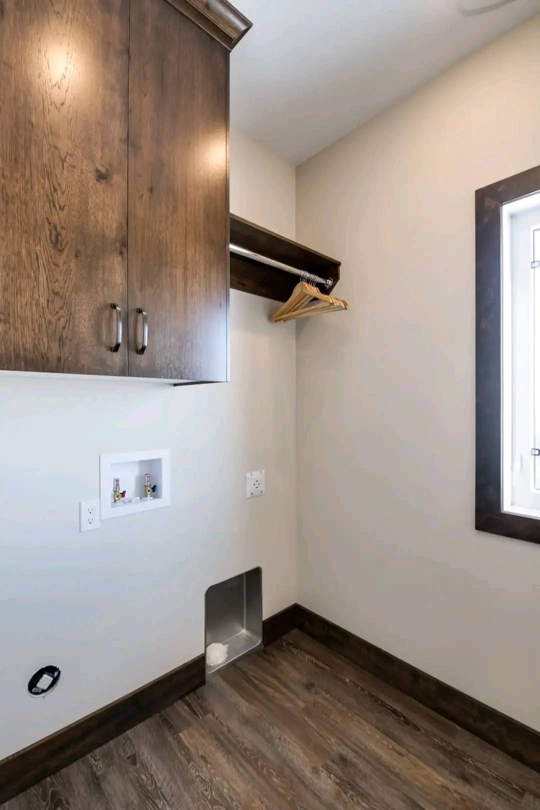 Laundry room with wooden cabinets, a shelf holding hangers, plumbing outlets for appliances, and a hardwood floor. The mood is clean and organized.
