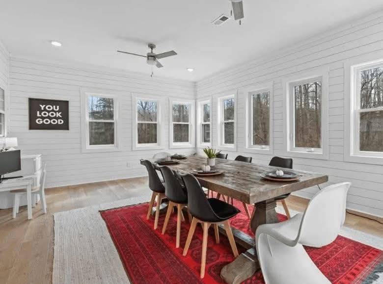 Stylish dining room with wooden table, black and white chairs on a red rug. White shiplap walls, large windows, and a playful "You Look Good" sign.