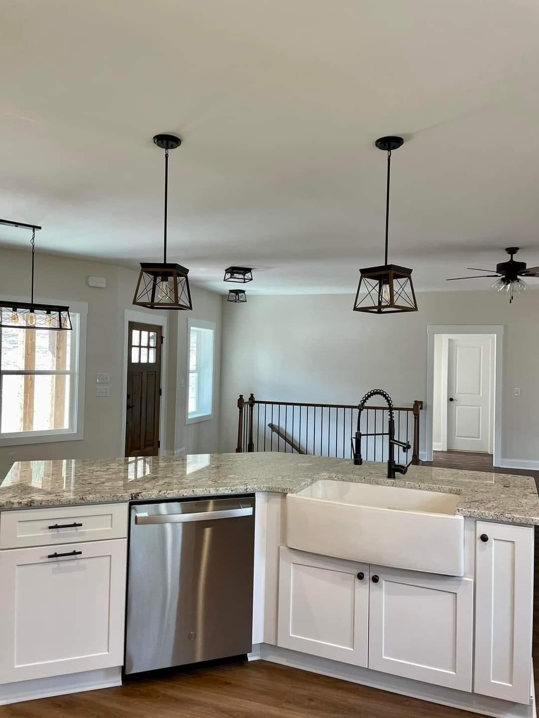Spacious kitchen with white cabinets, granite countertops, and a farmhouse sink. Pendant lights hang above, with light walls and wood flooring.