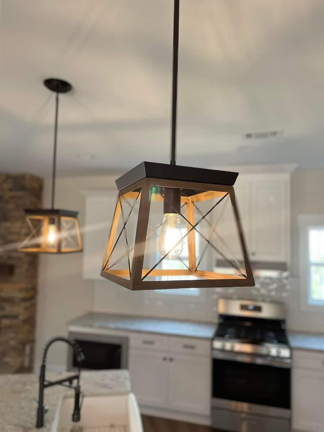Modern kitchen with two black metal and glass pendant lights hanging over a granite countertop. Stainless steel appliances in the background.