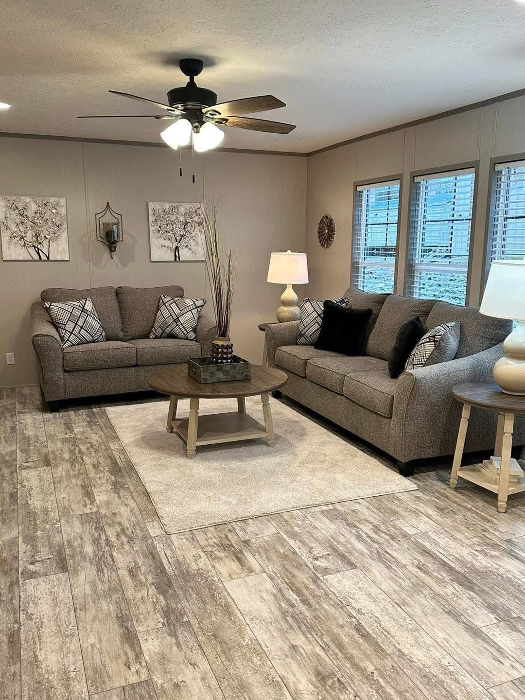 Modern living room with gray sofas, black and white cushions, wooden coffee table, soft lighting from lamps, art on beige walls, and wood flooring.