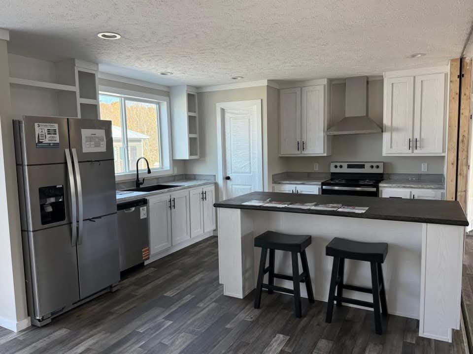 Modern kitchen with sleek, stainless steel appliances, white shaker cabinets, and a dark island with two black stools, exuding a contemporary vibe.