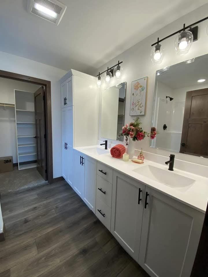Modern bathroom with double white vanity, black fixtures, and large mirrors. A vase of pink flowers and a rolled towel adorn the countertop.