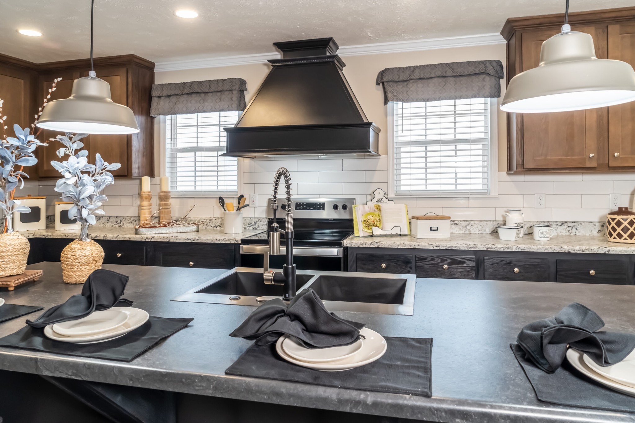 Modern kitchen with a large island, black countertop, and sink. Hanging lights and elegant place settings create a cozy, welcoming atmosphere.
