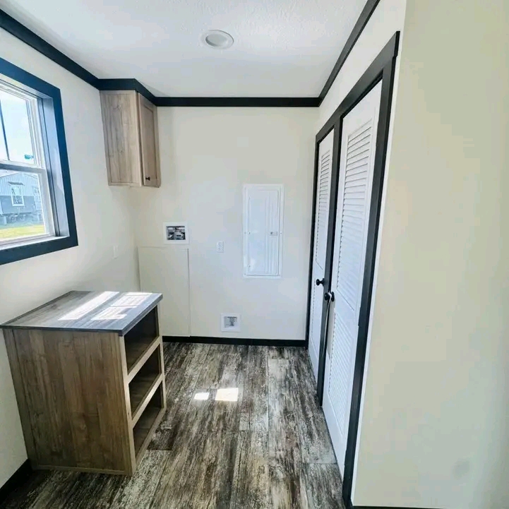 A small, bright room with wood-look flooring, a wood cabinet, white walls, black trim, a window, and two white doors, conveys simplicity and neatness.