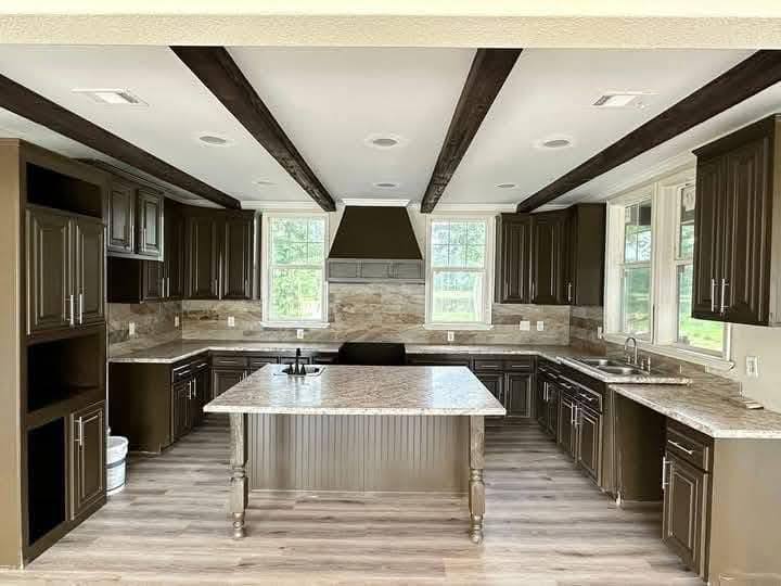 Spacious kitchen with dark wood cabinets, large island, and marble countertops. Exposed beams and large windows create an open, airy feel. Modern and elegant.