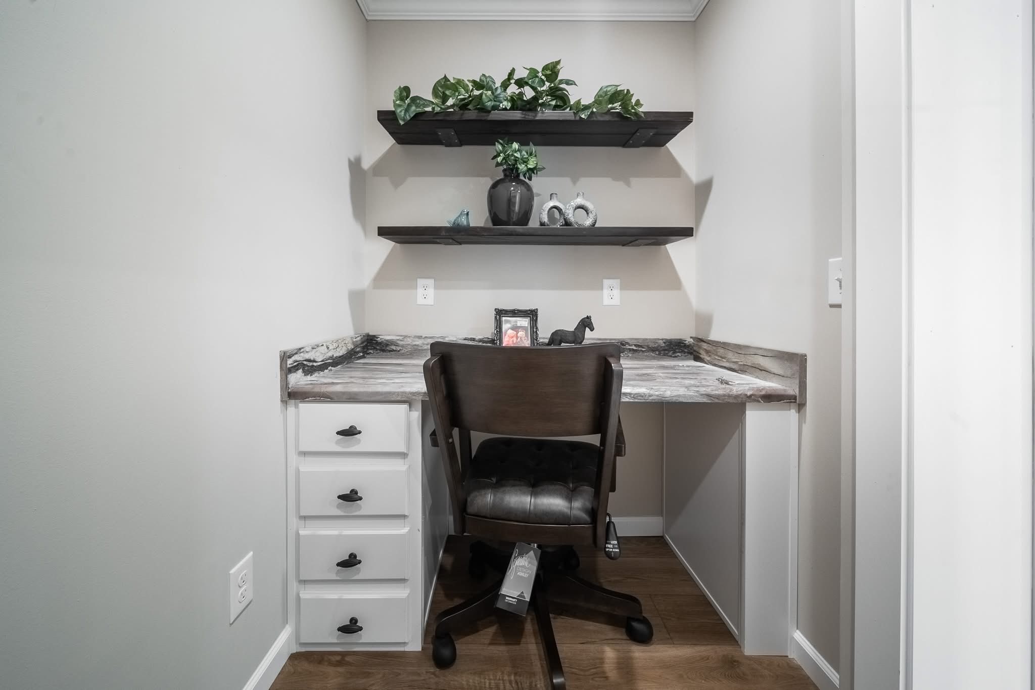 Cozy home office nook with a marble desk, dark wooden chair, and floating shelves adorned with plants and decorative items, creating a calm atmosphere.