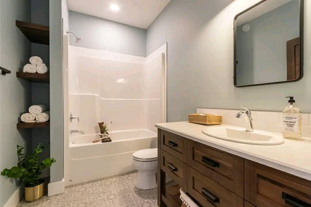 Modern bathroom with a corner bathtub, wood vanity with sink, and wall mirror. Shelves hold rolled towels and a plant, creating a serene, tidy ambiance.