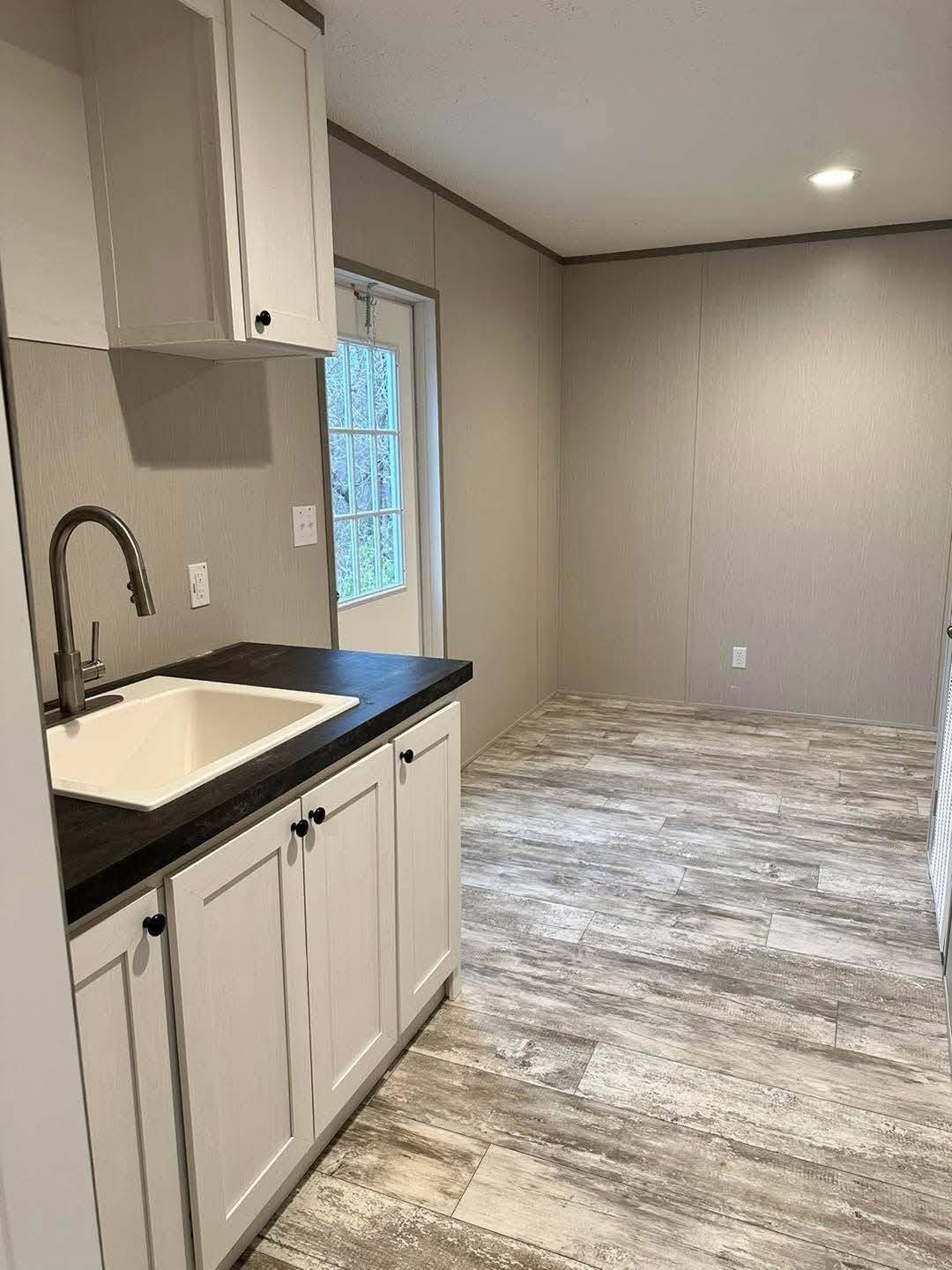 Minimalist utility room with light gray walls and textured flooring. Features a white cabinet with a black countertop and sink. Bright and clean ambiance.