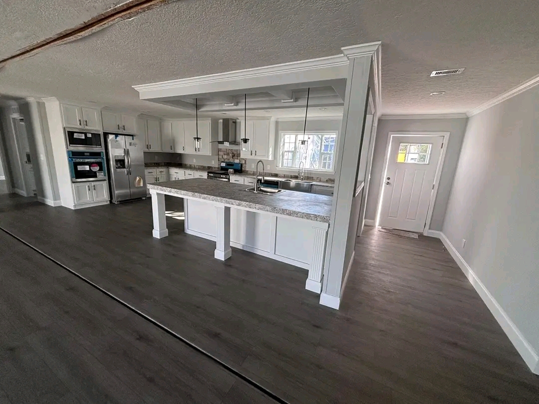 Modern kitchen with white cabinets and an island featuring pendant lights. Gray wood flooring and stainless steel appliances create a sleek, bright space.