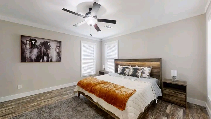 A cozy bedroom features a queen bed with star-patterned pillows and an orange throw blanket. A ceiling fan, warm lighting, and horse artwork add style.