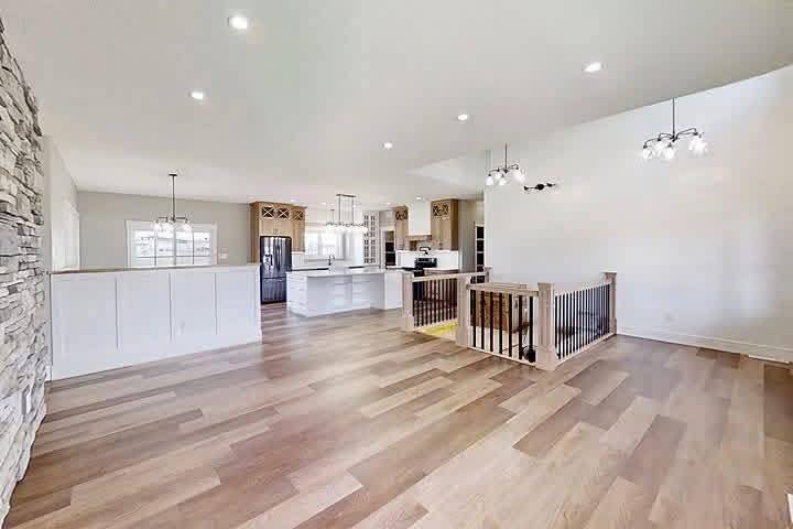 Modern open-concept living space with light wood flooring, white walls, and stone accent. Features kitchen island, pendant lights, and railing. Bright and airy.