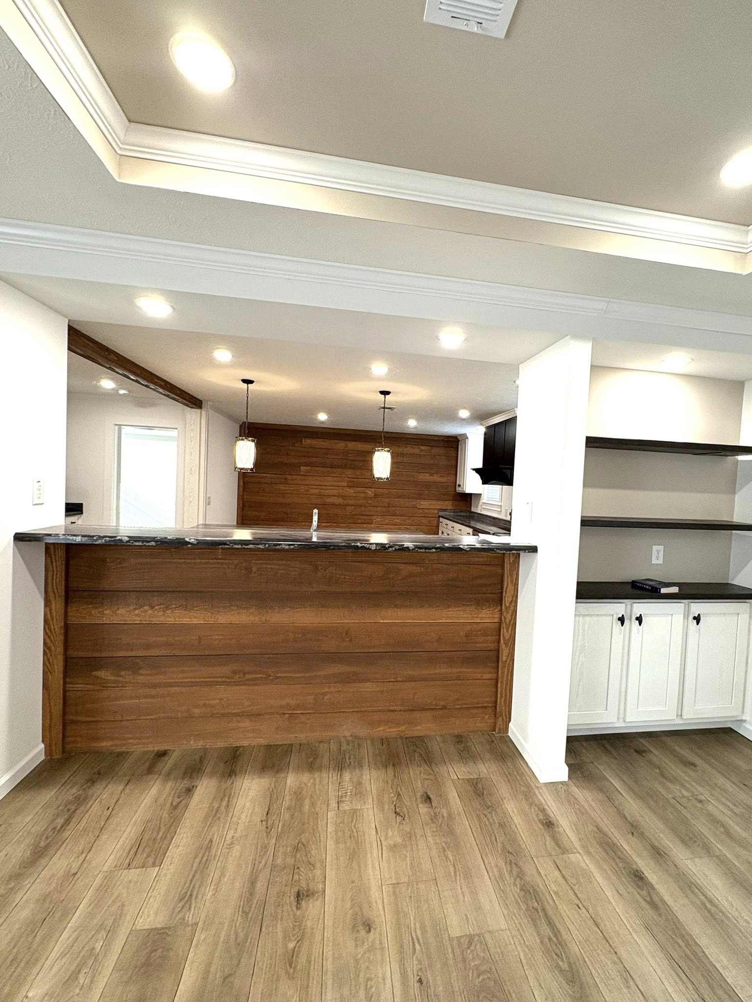 Modern kitchen with wood accents, open shelves, and pendant lights over a dark countertop. Light wood flooring enhances the warm, inviting atmosphere.