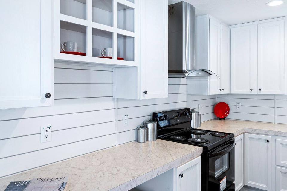 Bright, modern kitchen with white cabinets and countertops, featuring a black stove and stainless steel hood. Red accents add contrast and warmth.