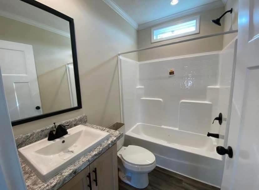 Modern bathroom with white fixtures, featuring a large framed mirror above a granite countertop with a sink. A bathtub with shower is on the right.
