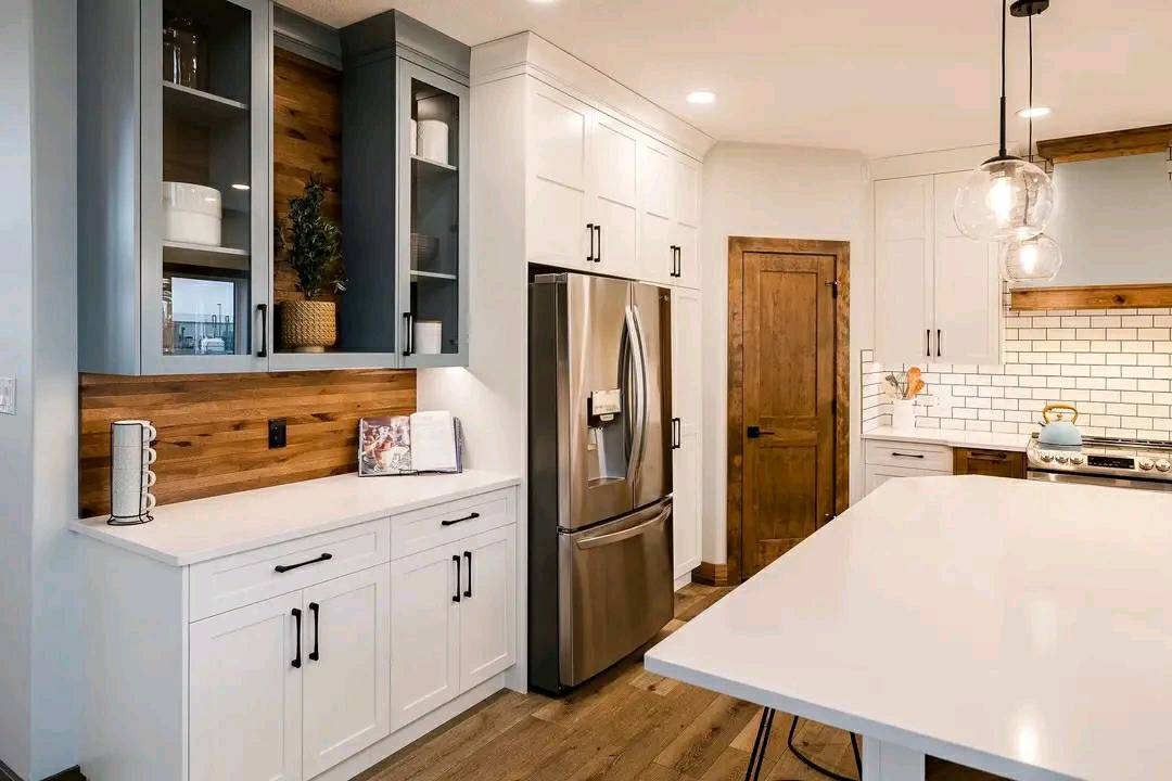 Modern kitchen with white cabinets, stainless steel fridge, and wooden accents. Tile backsplash and pendant lights create a warm, inviting atmosphere.