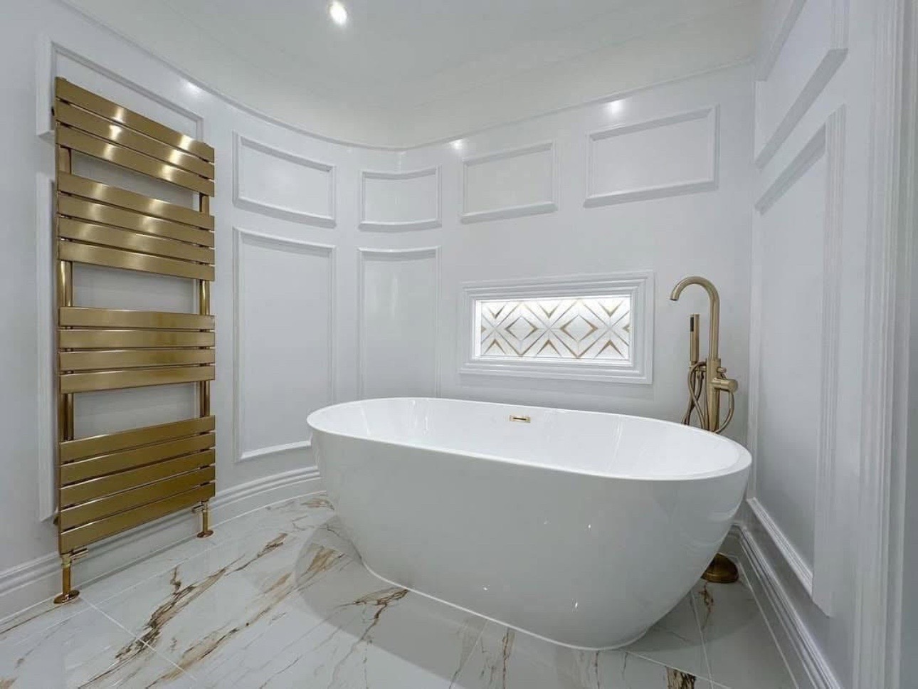 Luxurious bathroom with a sleek white bathtub, gold faucet and towel rack, marble floor, and decorative window, creating a serene, elegant ambiance.