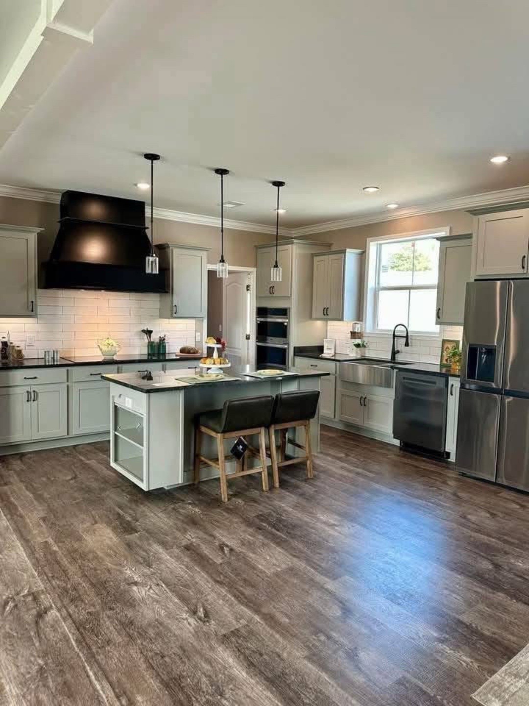 Spacious modern kitchen with gray cabinets, dark wood flooring, and a central island with stools. Stainless steel appliances and pendant lights create a sleek, inviting atmosphere.