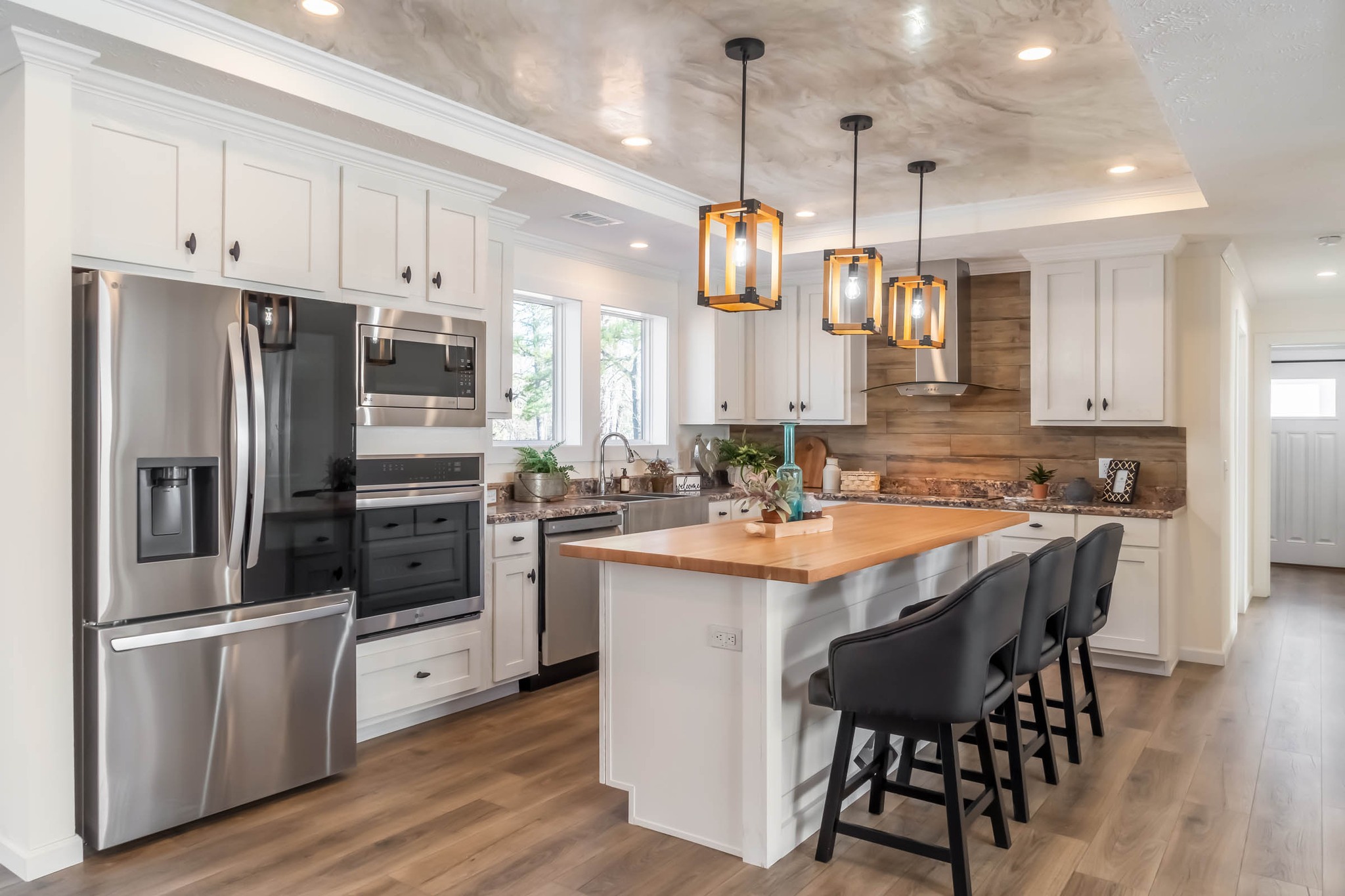 Modern kitchen with white cabinets, stainless steel appliances, and a wooden island with black chairs. Warm pendant lights add elegance and coziness.