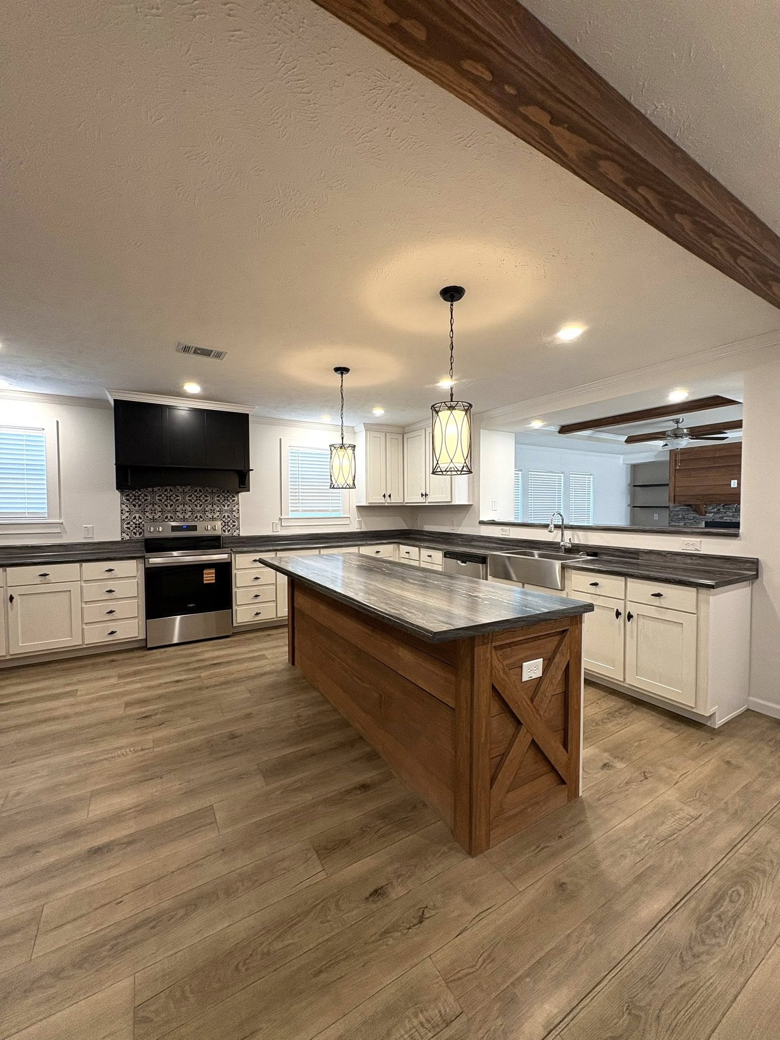 Spacious kitchen with a wooden island, pendant lights, and stainless steel appliances. White cabinets, light wood flooring, and a warm, inviting atmosphere.