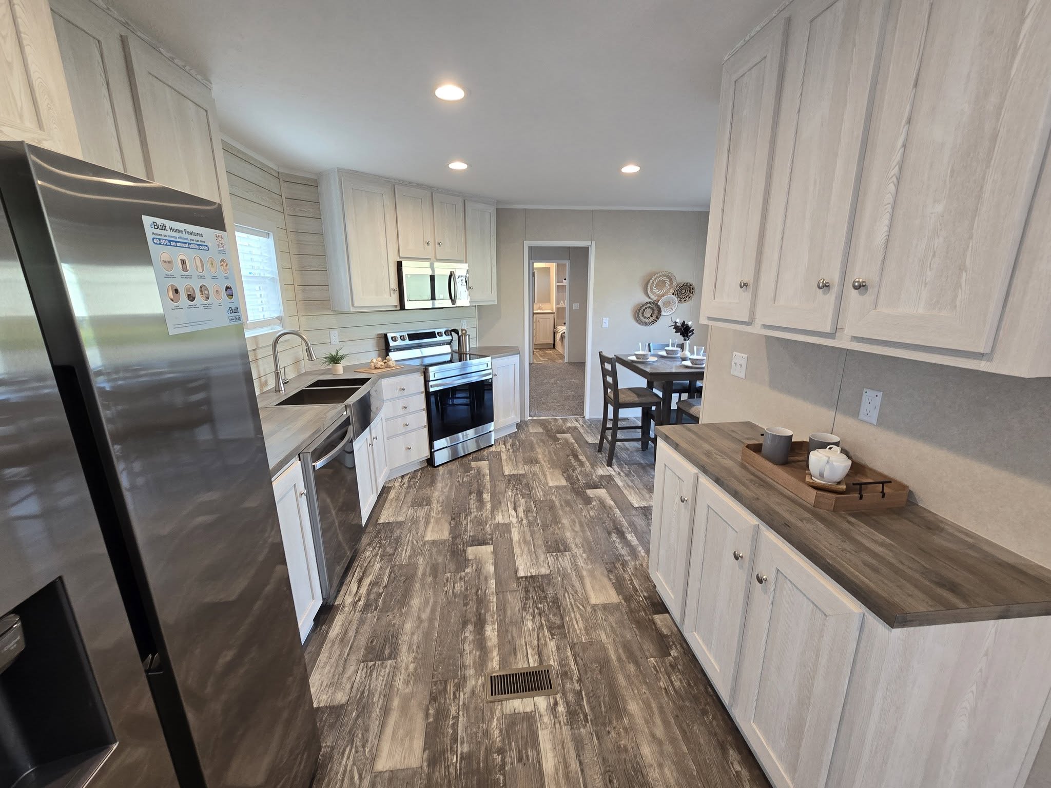 Modern kitchen with white cabinets, stainless steel appliances, and wood-patterned flooring. Dining area with a set table is visible through a doorway.