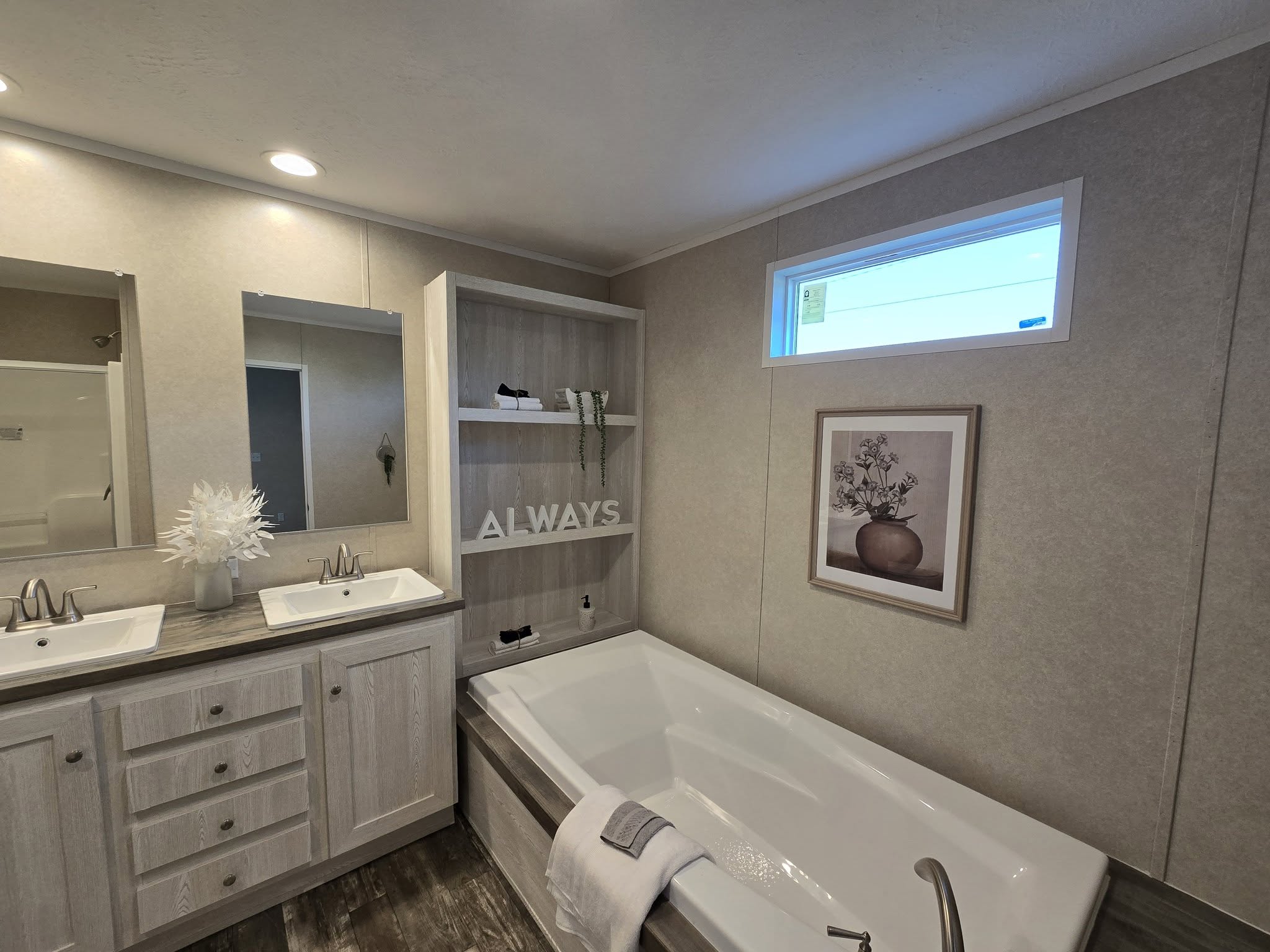 Modern bathroom with dual sinks, a large bathtub, a towel draped over the edge, and open shelving. Decor is minimal with neutral tones and a calming vibe.