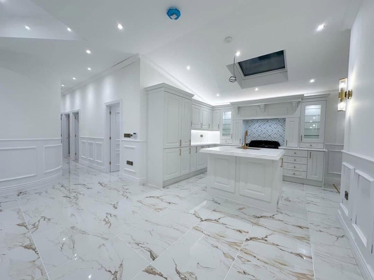 Spacious modern kitchen with white cabinets, island, and marble floor. Soft lighting and skylight create an airy feel. Elegant and serene ambiance.