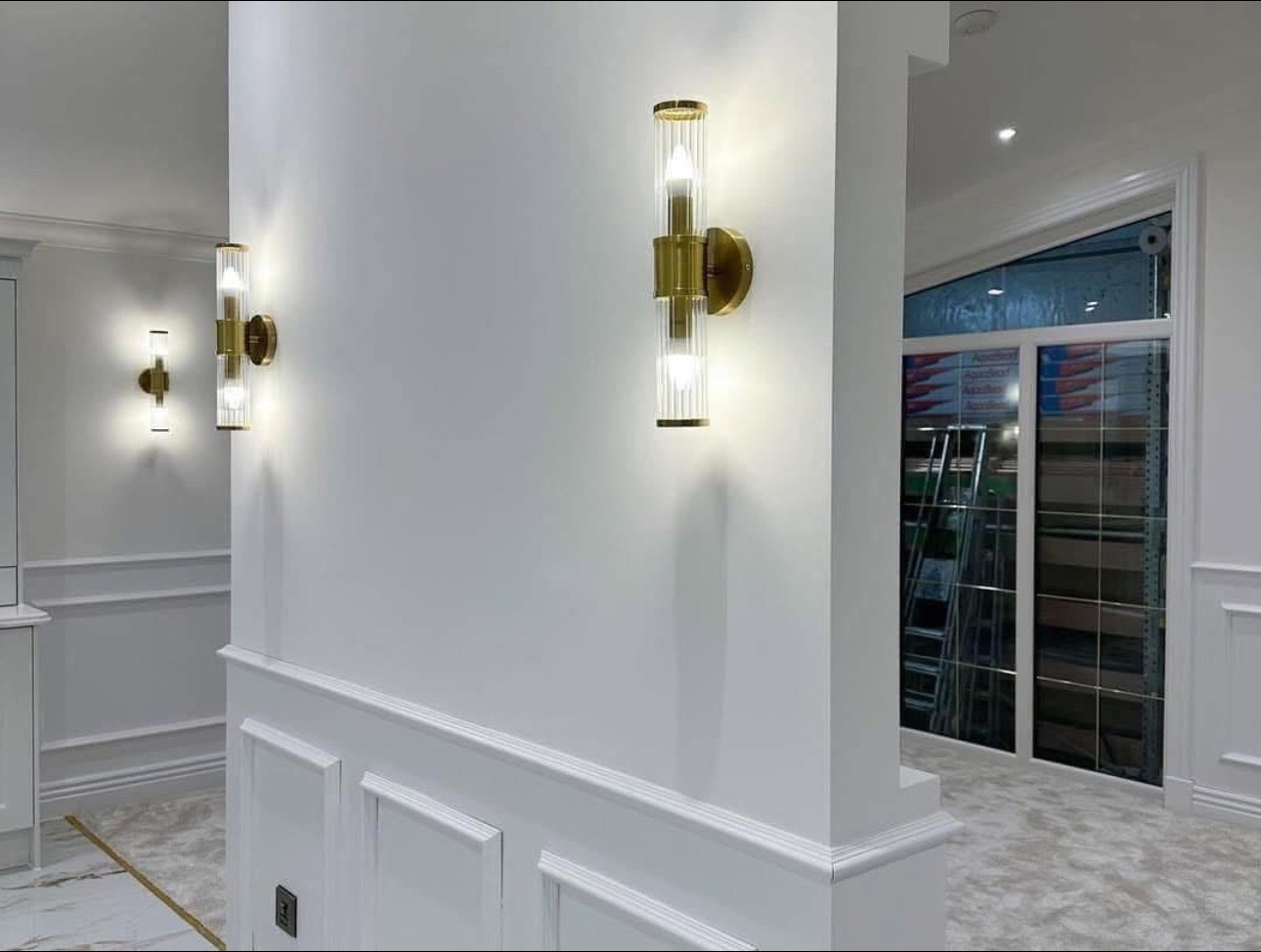 Bright modern interior with elegant wall sconces on white walls, featuring gold fixtures and soft lighting. Clean, sophisticated, and minimalist design.