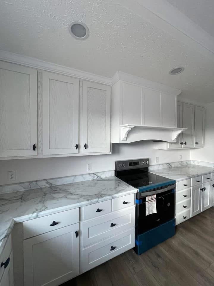 Spacious kitchen with white cabinets, marble countertops, and a stainless steel stove wrapped in blue protective film. Wood flooring adds warmth.