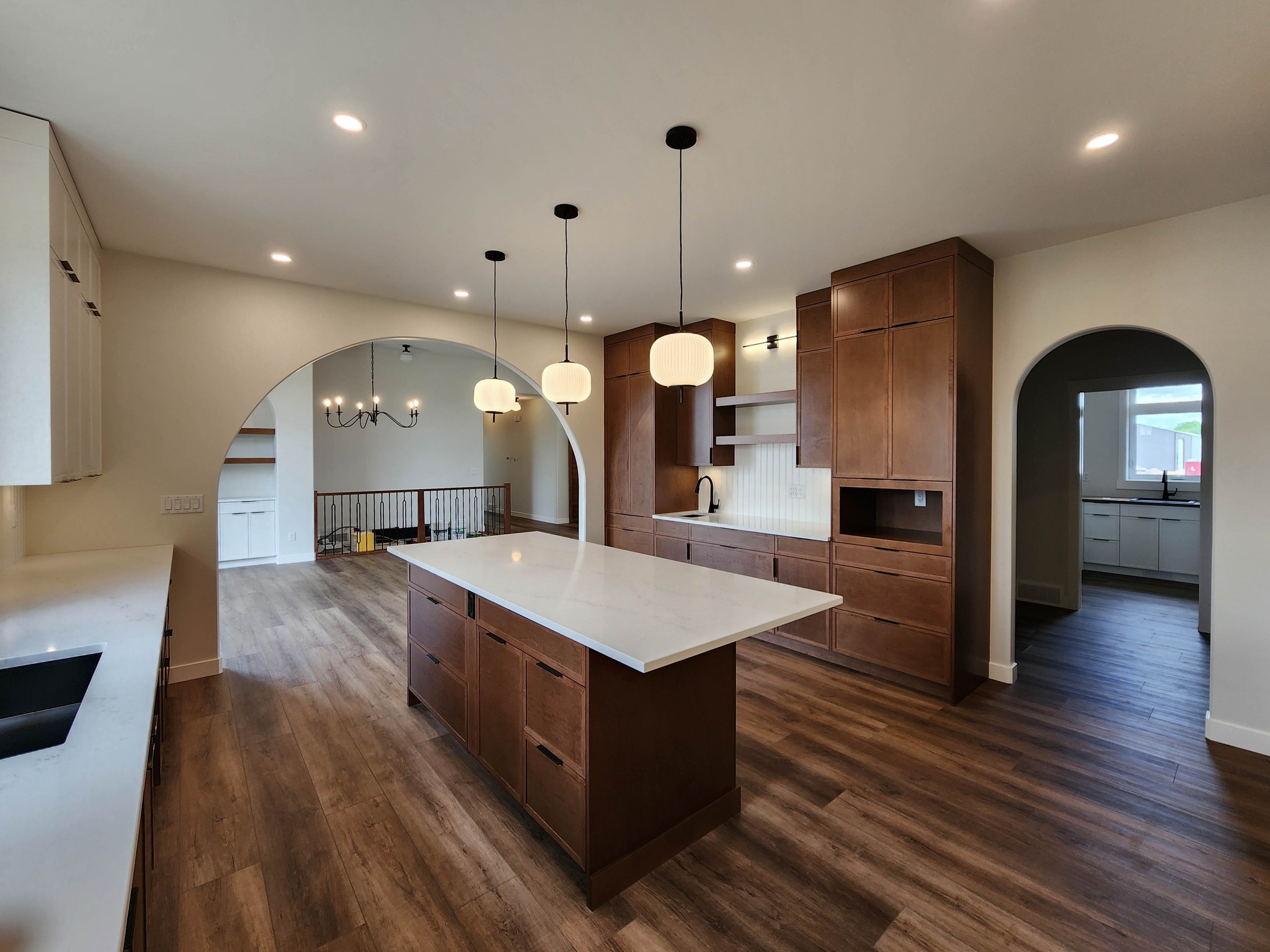 Spacious kitchen with wooden floors, a large island countertop, and modern pendant lights. Arched doorways lead to adjacent rooms, evoking an elegant tone.