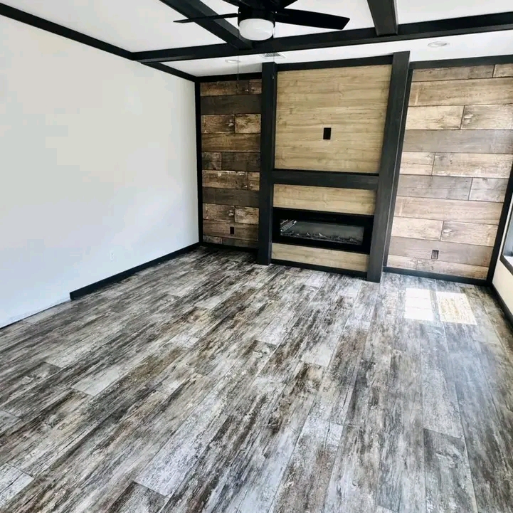 Minimalist room with rustic wood flooring and matching accent walls. A modern black ceiling fan is overhead. Natural light filters through a window.