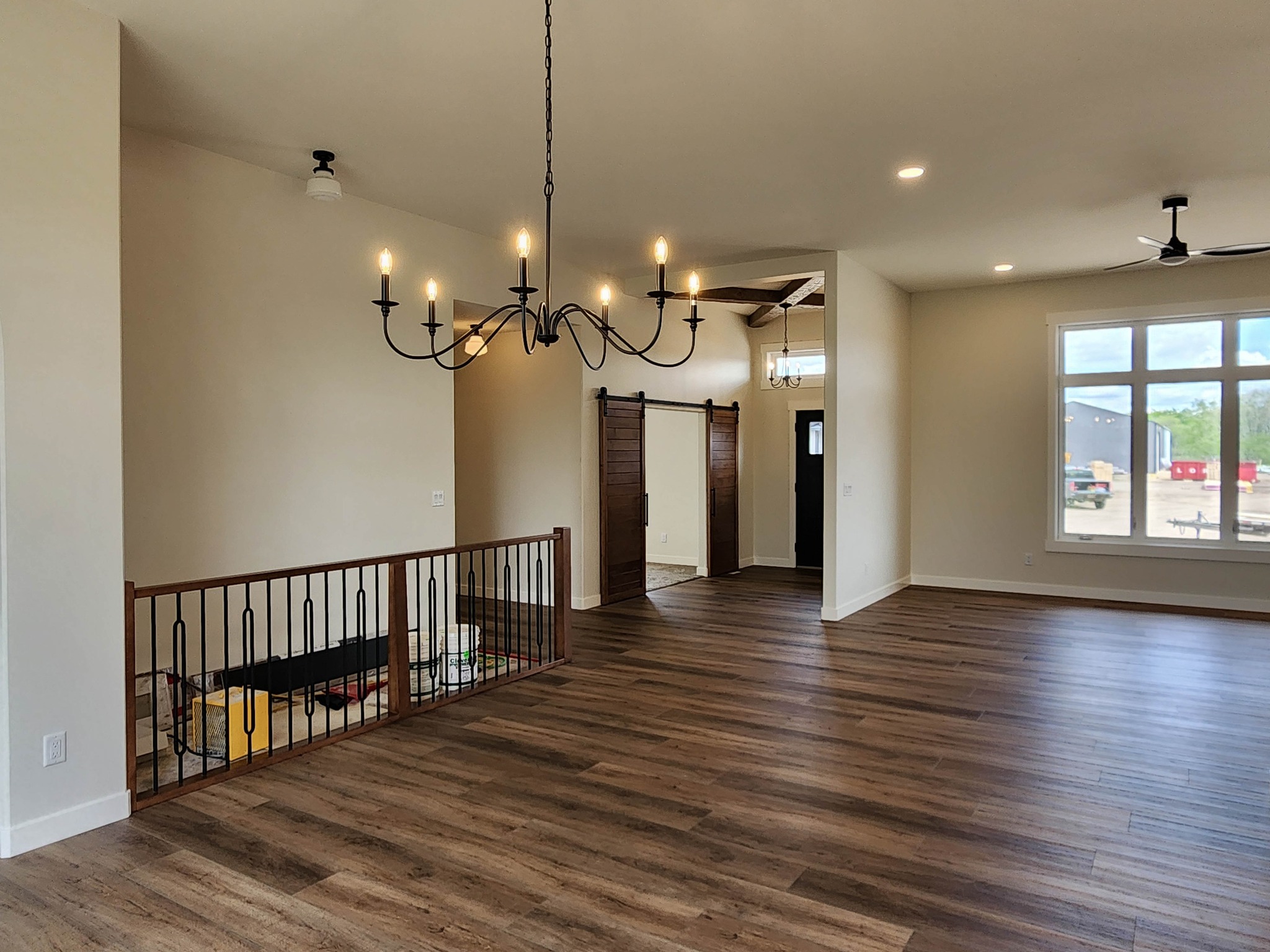 Spacious living area with wood floors, large window, and candle-style chandelier. Includes barn doors and iron railing, conveying a rustic, open ambiance.
