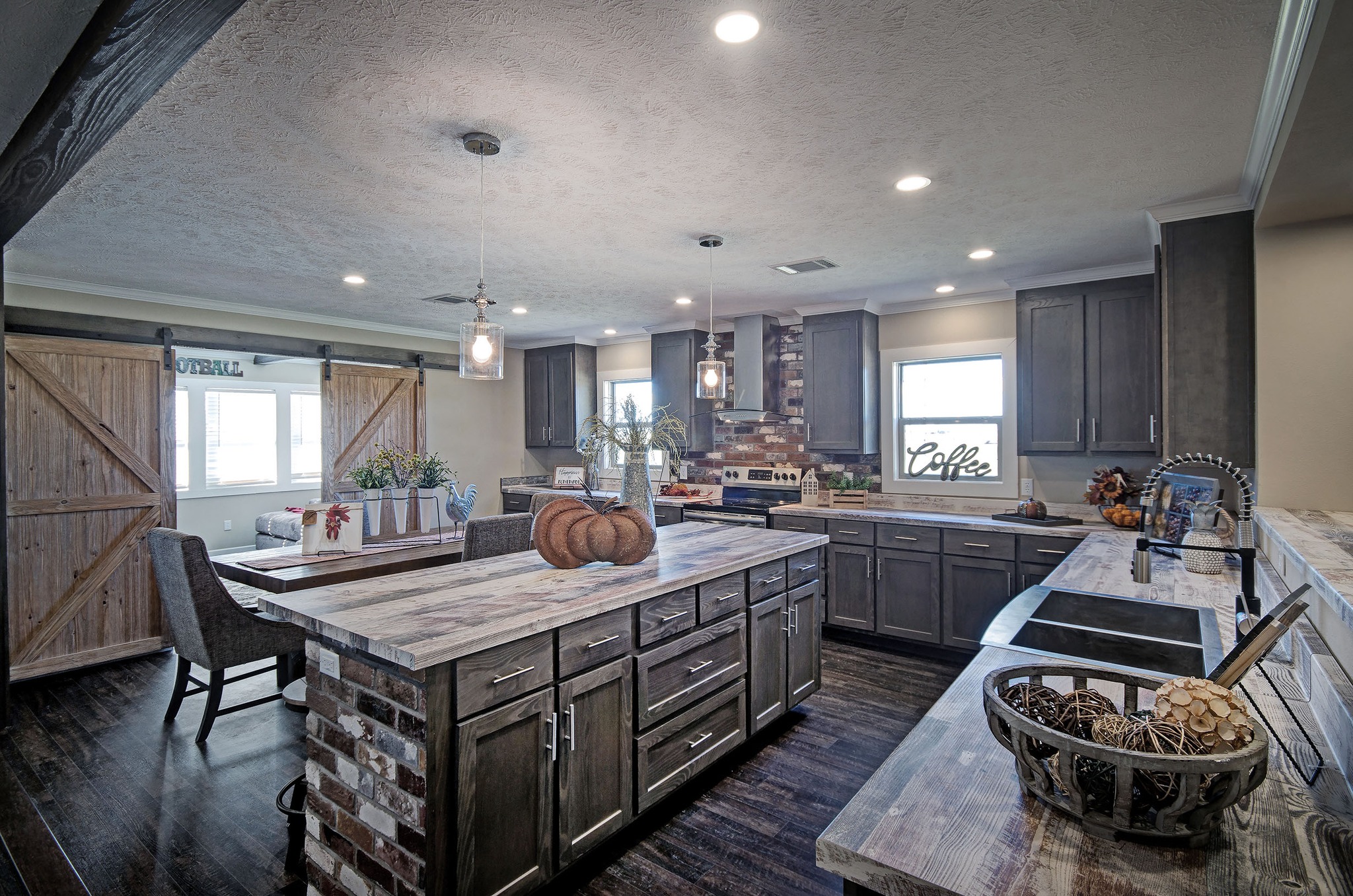 Spacious, rustic kitchen with dark wood cabinets, large island, and farmhouse sink. Decor includes pumpkins and a "Coffee" sign. Cozy, inviting vibe.
