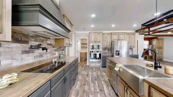 Modern kitchen with a sleek design features dark cabinets, stainless steel appliances, and a large island with a farmhouse sink. The space is bright and inviting with wood-look flooring and recessed lighting.