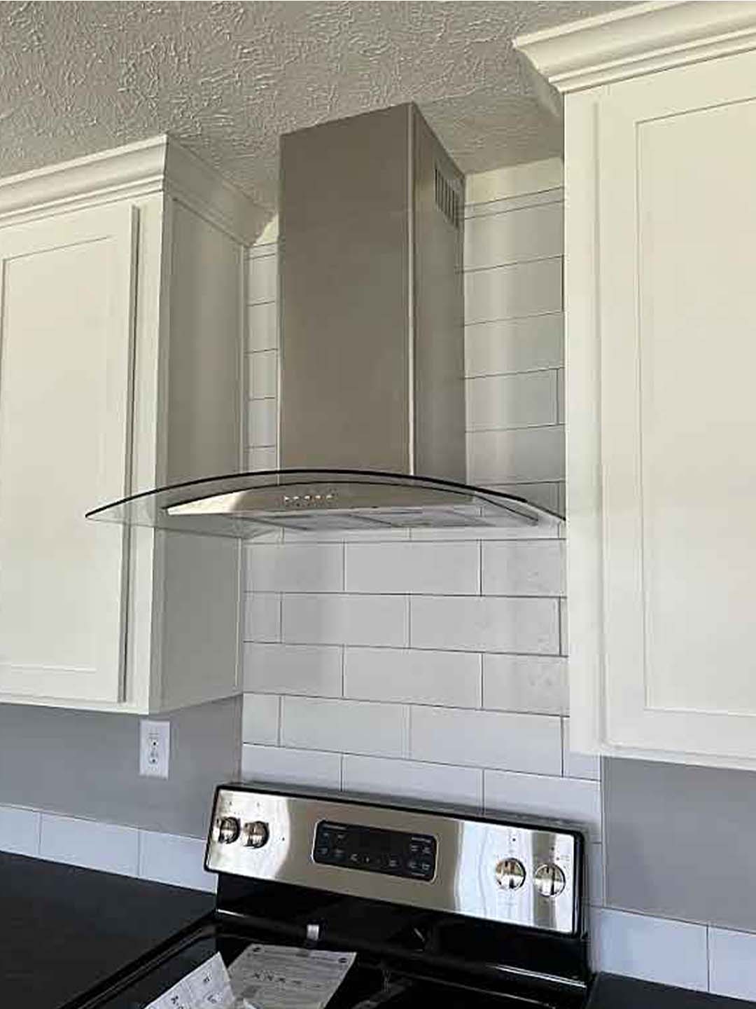 Modern kitchen with a sleek stainless steel range hood above a black stove. White cabinets and subway tile backsplash provide a clean, contemporary feel.