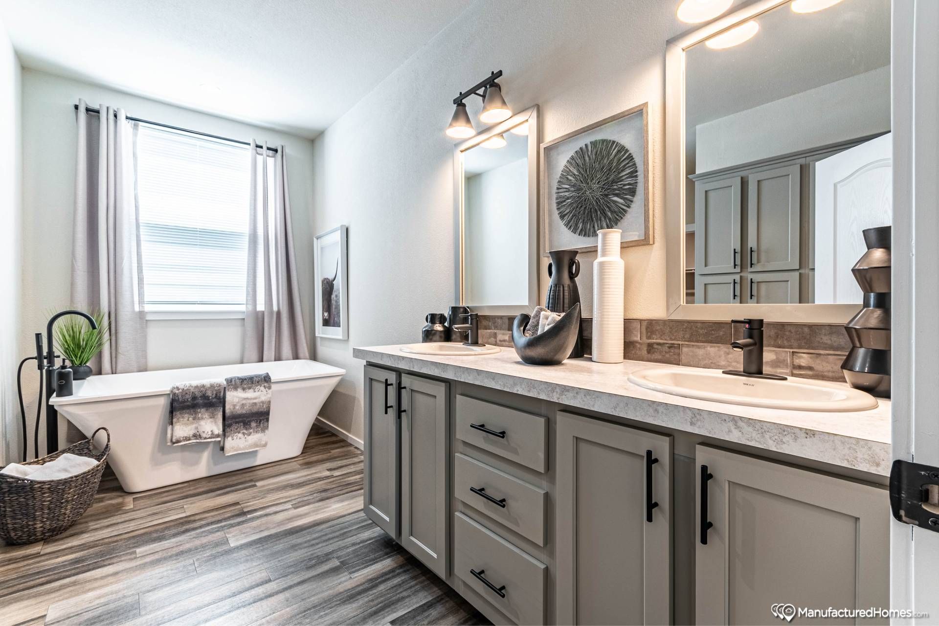 Modern bathroom with dual sinks on a marble countertop, large mirrors, and stylish decor. A sleek freestanding tub sits by a window with soft drapes, conveying elegance.