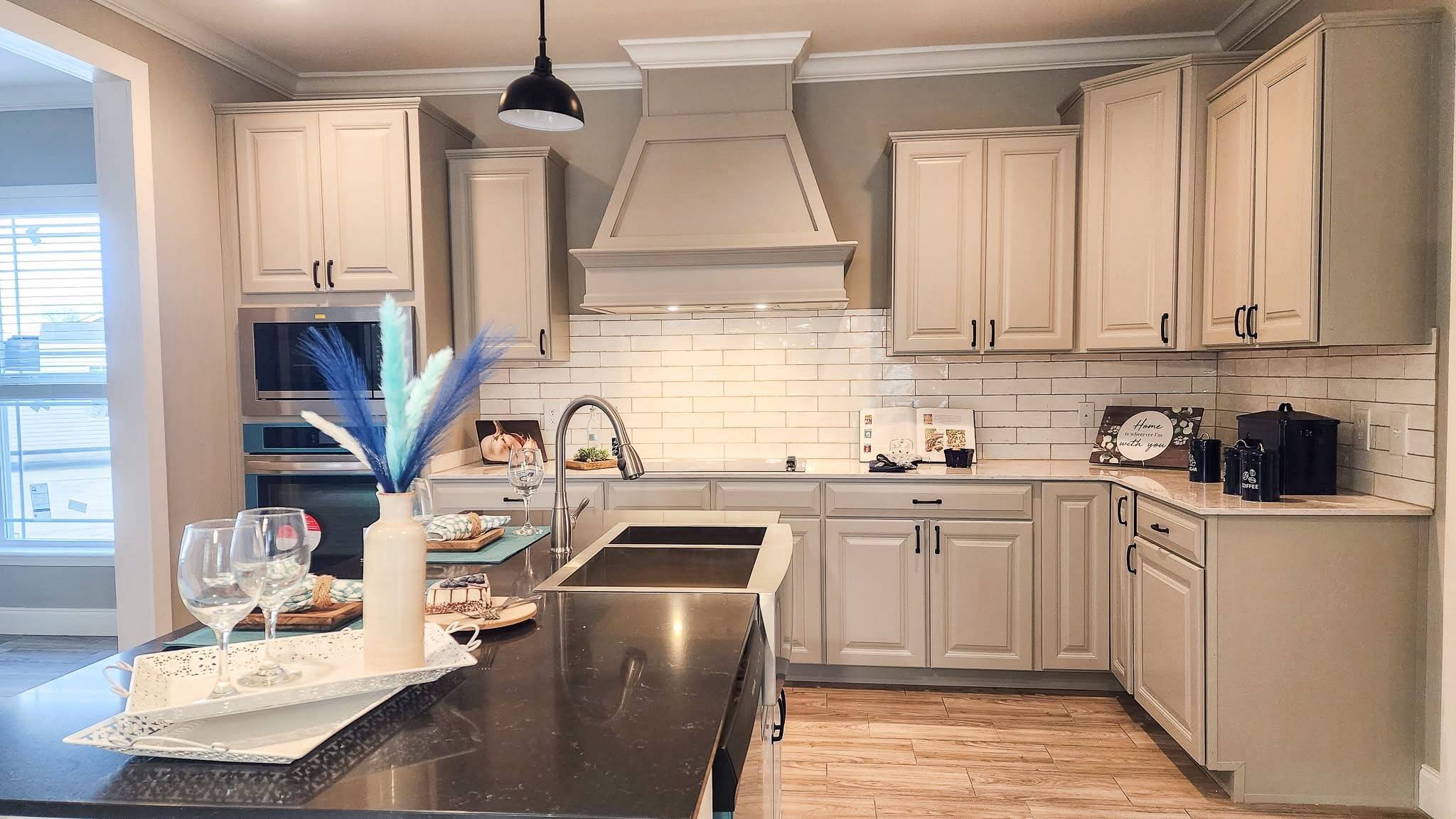 Modern kitchen with beige cabinets, white subway tile backsplash, and a central black countertop island. A vase with blue and white feathers adds elegance.