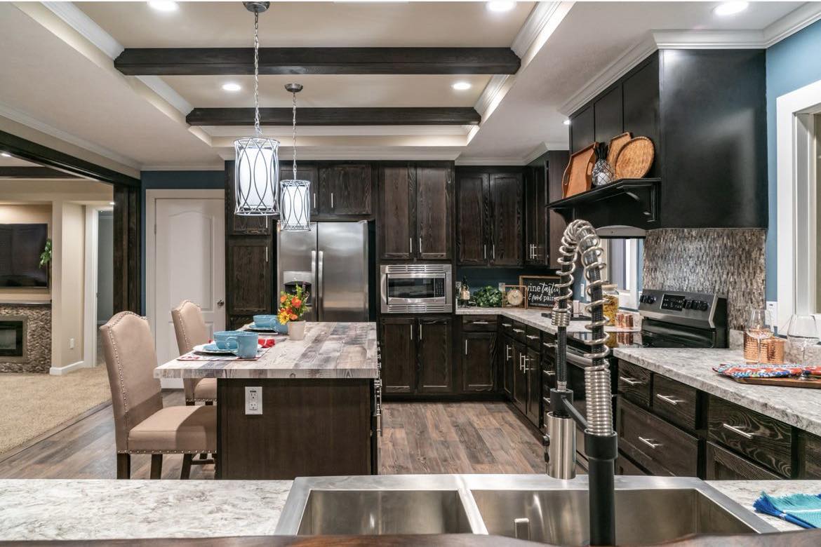 Modern kitchen with dark wood cabinets, marble countertops, and an island with beige chairs. Pendant lights hang above. Warm, inviting atmosphere.